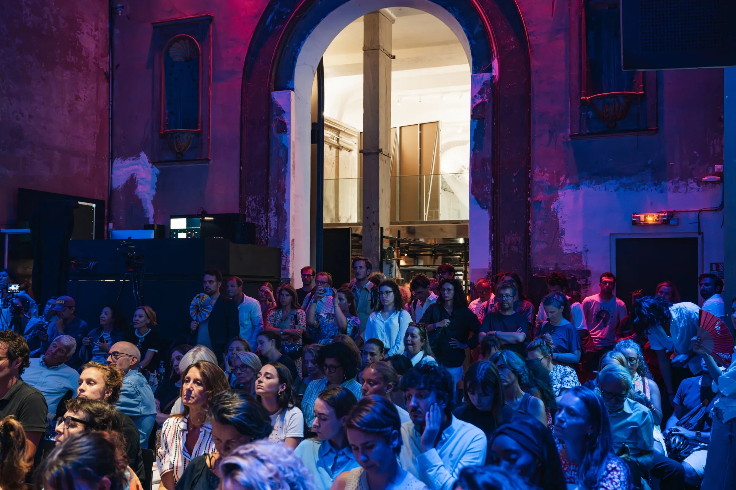 Le public dense dans la grande salle du Café A, sous la voûte, dans la lumière bleue et rose.
