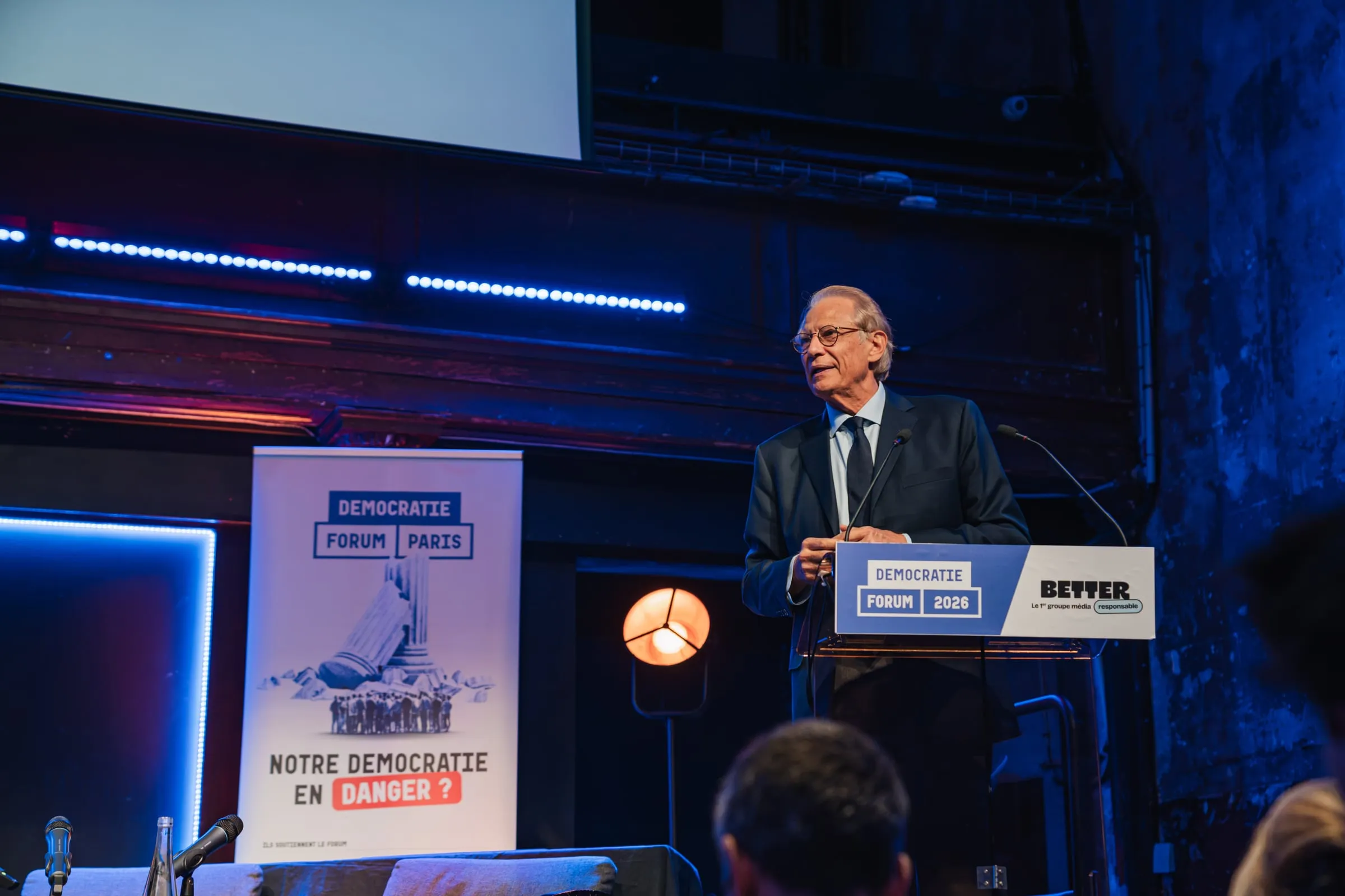 Dominique de Villepin au pupitre du forum, à côté du kakémono « Notre démocratie en danger ? ».